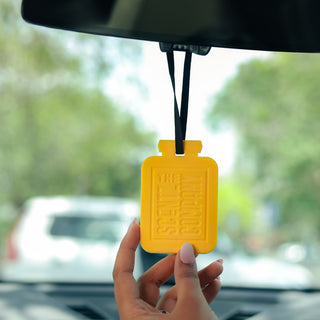 Yellow car air freshener held in front of a car's rearview mirror.
